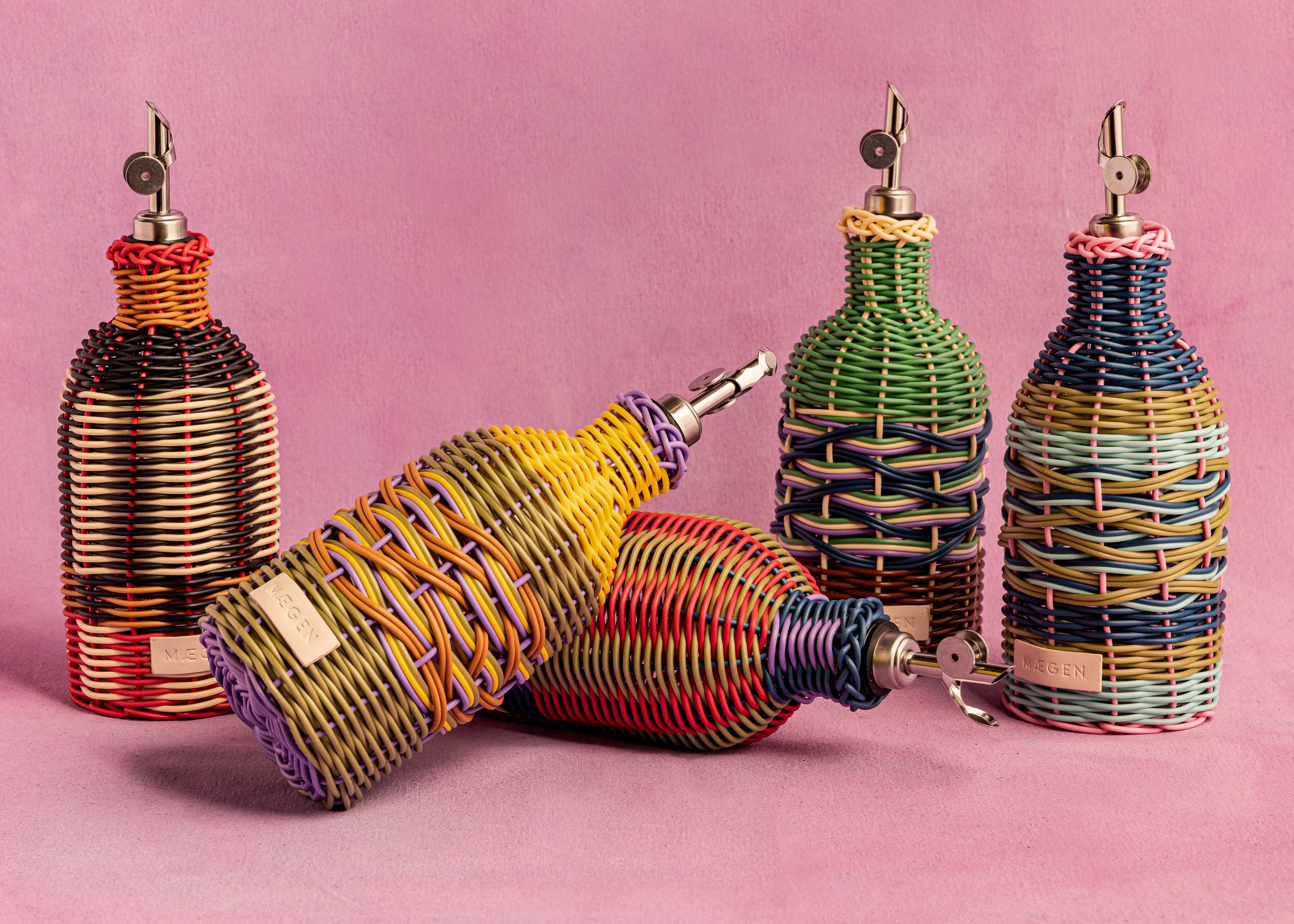 Colorful woven bottles with metallic nozzles on a pink background