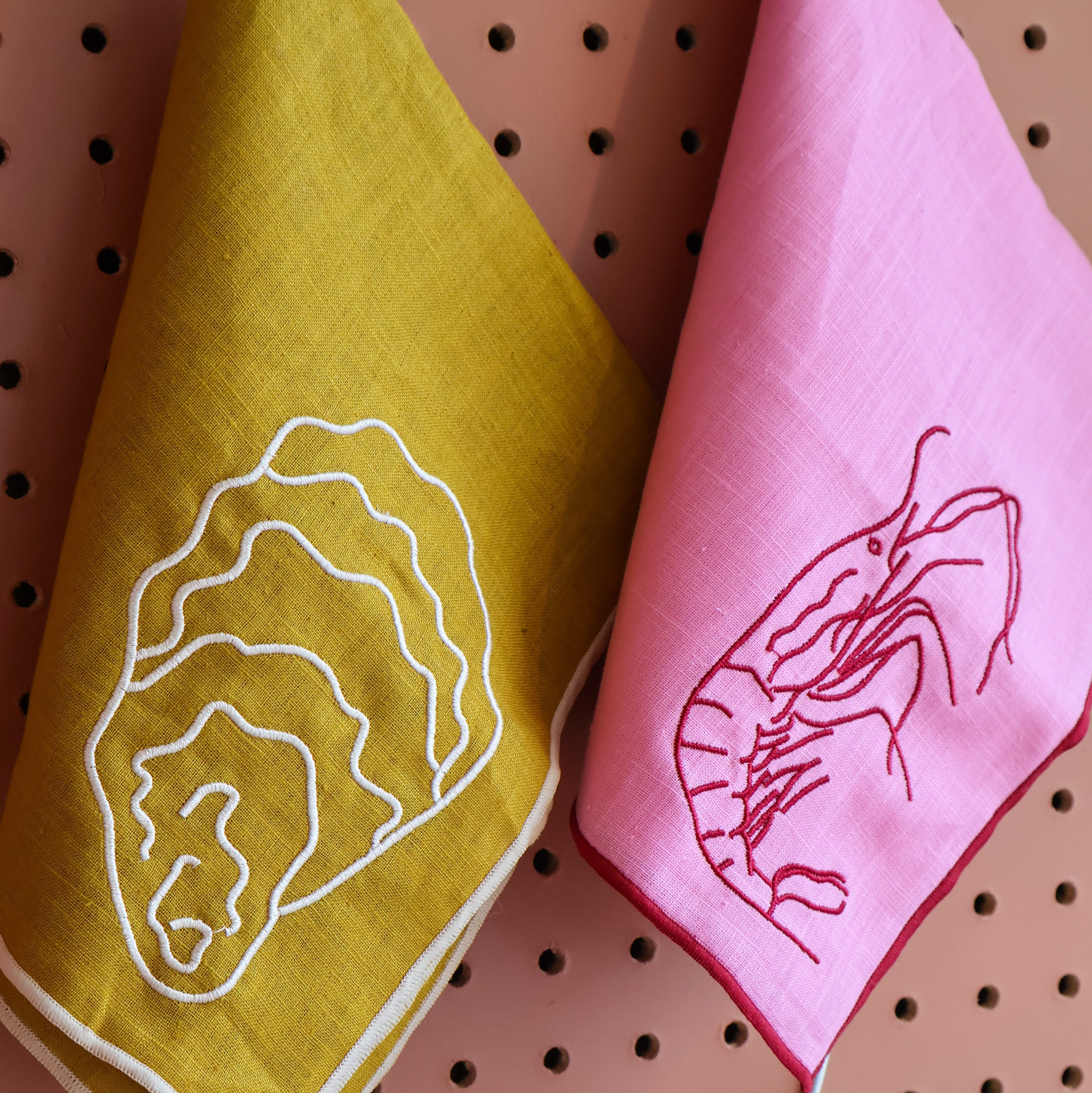 Yellow and pink towels with embroidered designs on a pegboard background