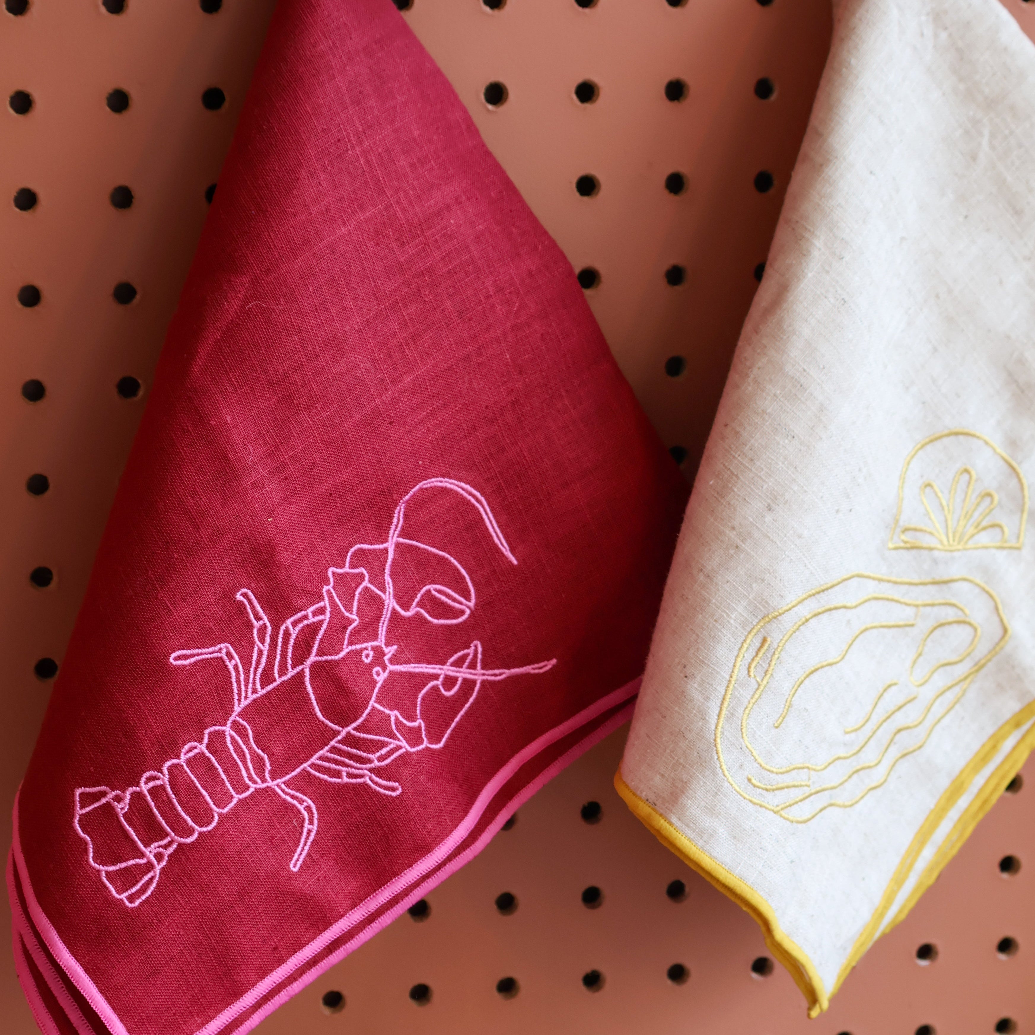 Napkins with lobster and oyster designs hanging on a pegboard.