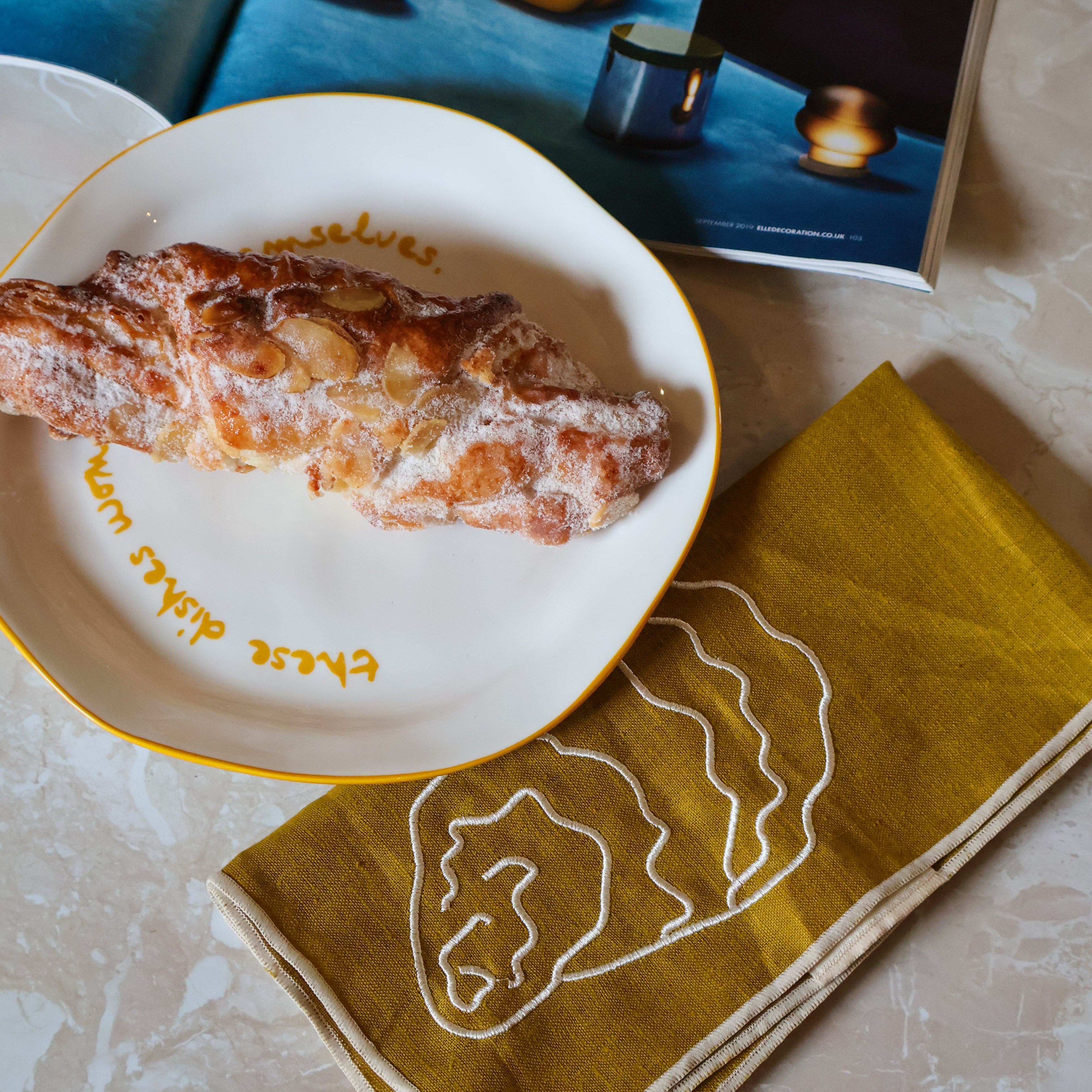Pastry on a plate with a magazine and OCA X MAEGEN napkin