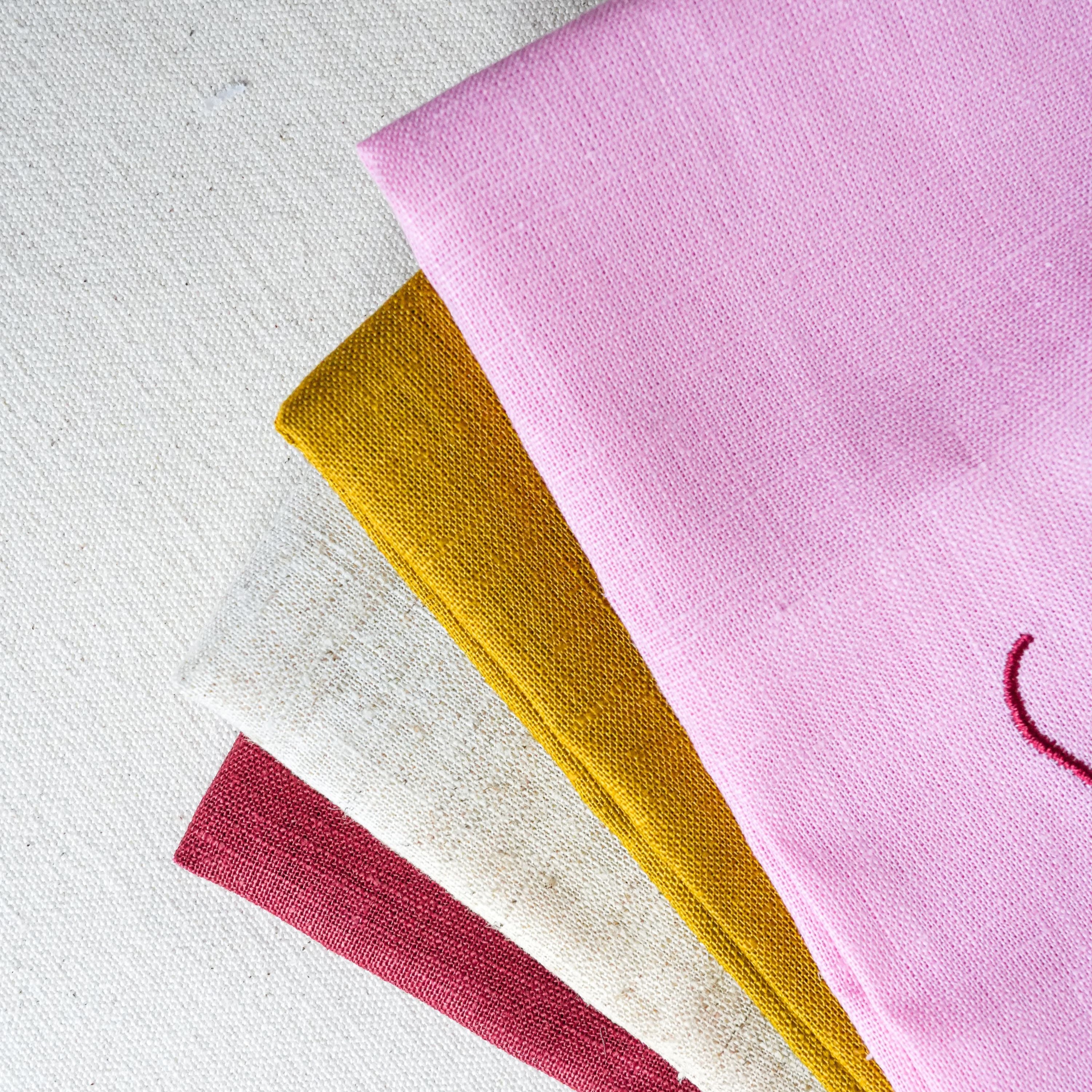 Four close ups of the napkin fabric and colours in pink, mustard yellow, burgundy, and beige flecked linen blend.